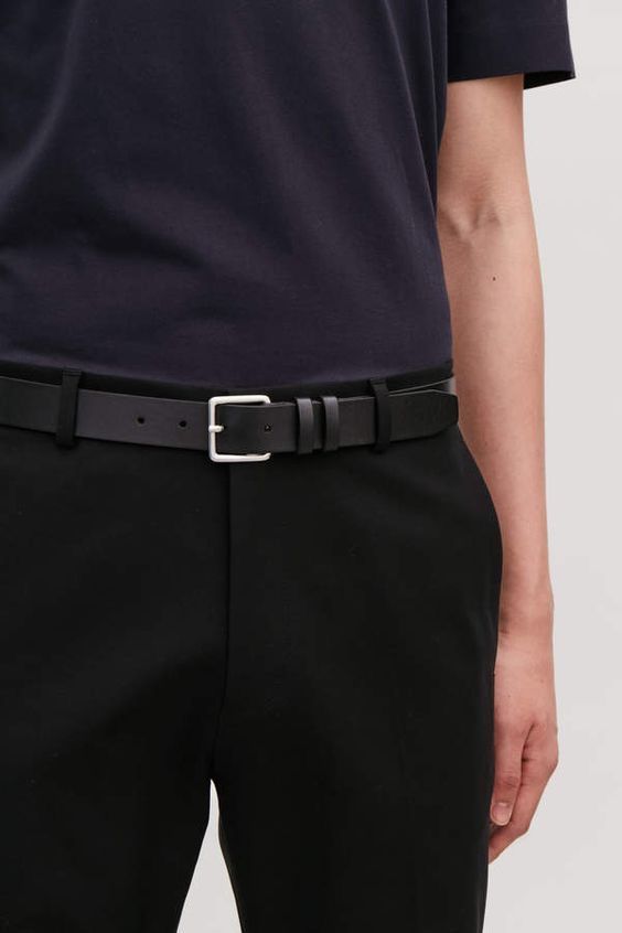 Person wearing a black belt with a silver buckle on a plain background